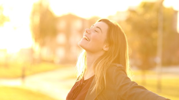 Back light portrait of a happy single teen girl breathing fresh air at sunset in a park